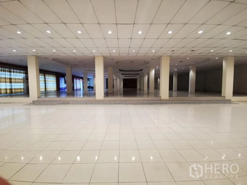 Retail Space for rent in Lam Luk Ka, Pathum Thani - Expansive tiled showroom interior with multiple columns, recessed lights and a raised platform area.