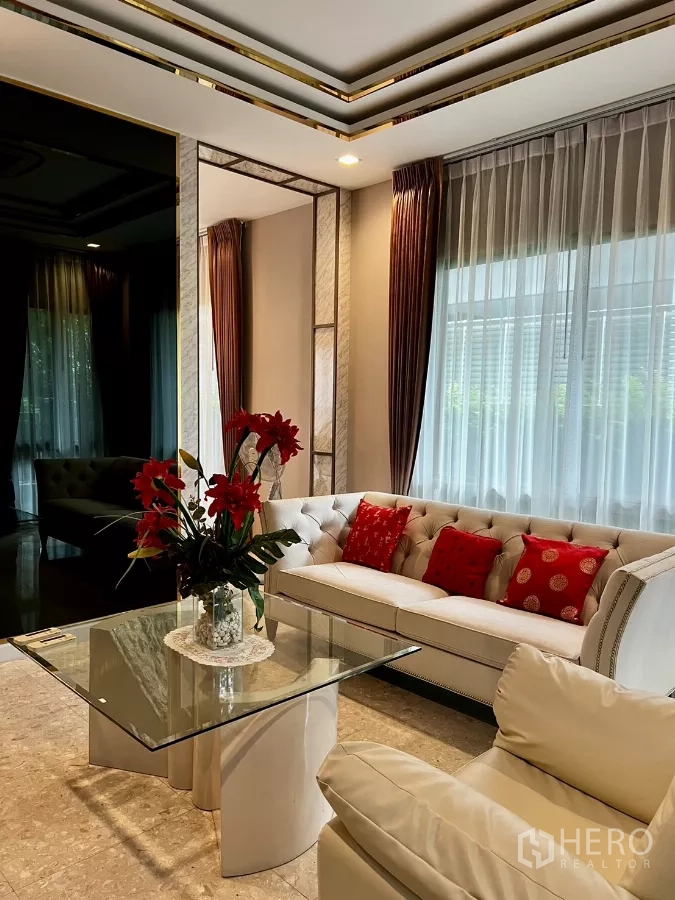Detached House for rent or sale in Prawet, Bangkok - Bright living room featuring a tufted sofa, glass coffee table and full-length curtains.