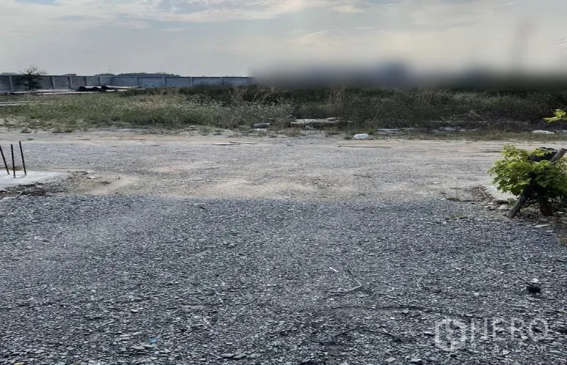 Land for sale in Sai Noi, Nonthaburi - Level land with compacted gravel surface and light vegetation, ready for development.