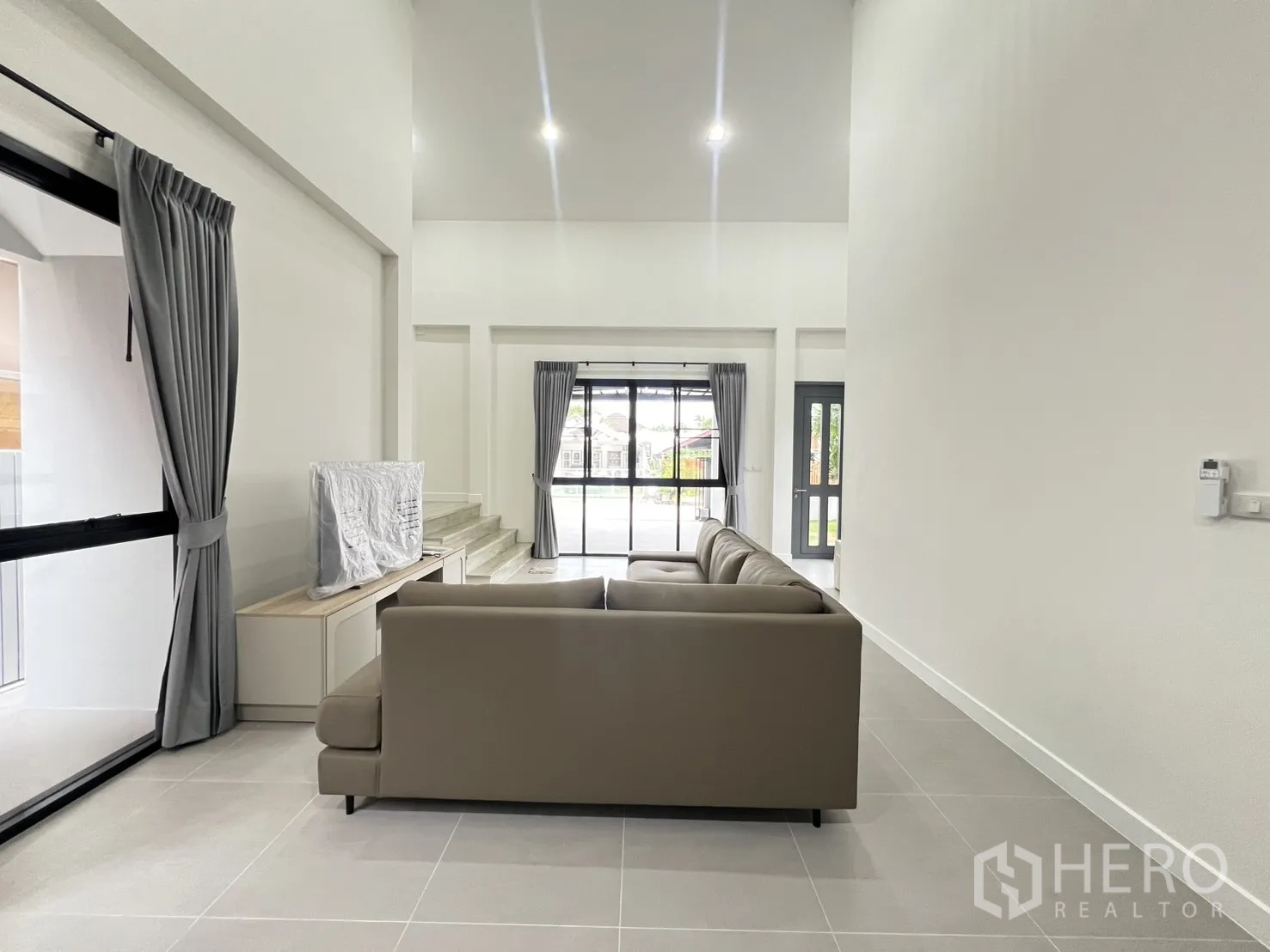 Detached House for rent in Saphan Sung, Bangkok - Open-plan living area with L-shaped sofa and tall windows at both ends.