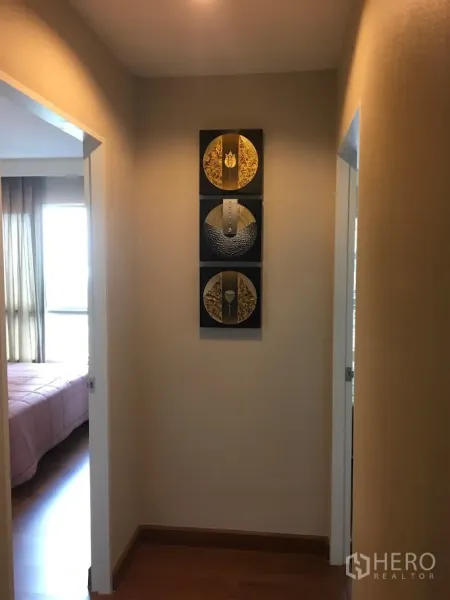 Condominium for rent in Huai Khwang, Bangkok - Well-lit hallway with wooden flooring and decorative wall art leading to two bedrooms.