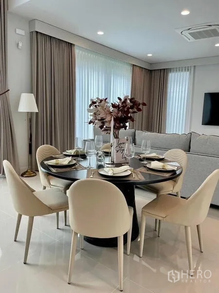 Detached House for rent or sale in Bang Kapi, Bangkok - Contemporary dining area with round table set for six beside curtains.