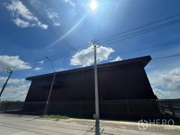 คลังสินค้า ให้เช่าในMin Buri, Bangkok - ด้านข้างโกดังหลังคาทรงจั่วขนาดใหญ่ มีรั้วรอบและสายไฟพาดเหนือศีรษะ