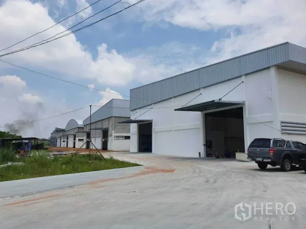 คลังสินค้า ให้เช่าในChon Buri - แถวโกดังสีขาวสมัยใหม่ในศรีราชา ประตูม้วนใหญ่ ชายคาเหล็ก และทางคอนกรีตกว้างสำหรับรถบรรทุก