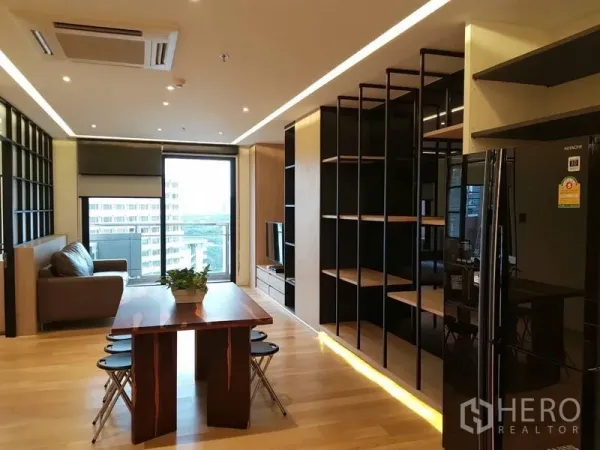 Condominium for rent in Bang Rak, Bangkok - Open-plan living and dining area with tall shelving, wood floors and balcony access.