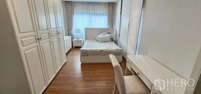 Detached House for rent in Bang Phli, Samut Prakan - Secondary bedroom with white wardrobes, work desk and soft daylight through sheer curtains.