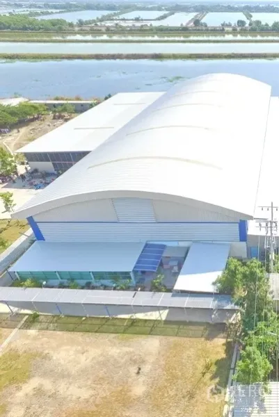 Warehouse for sale in Phra Samut Chedi, Samut Prakan - Aerial view of large metal-roof warehouse with fenced perimeter beside a canal.