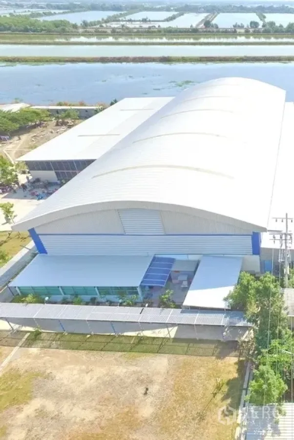 Warehouse for sale in Phra Samut Chedi, Samut Prakan - Aerial view of large metal-roof warehouse with fenced perimeter beside a canal.