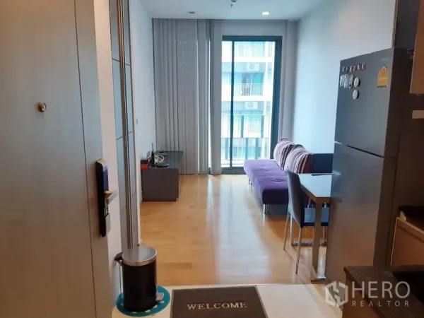 Condominium for sale in Khlong Toei, Bangkok - Bright living area with wood floors, purple sofa, dining table and sliding door to a balcony in a Khlong Toei condo.
