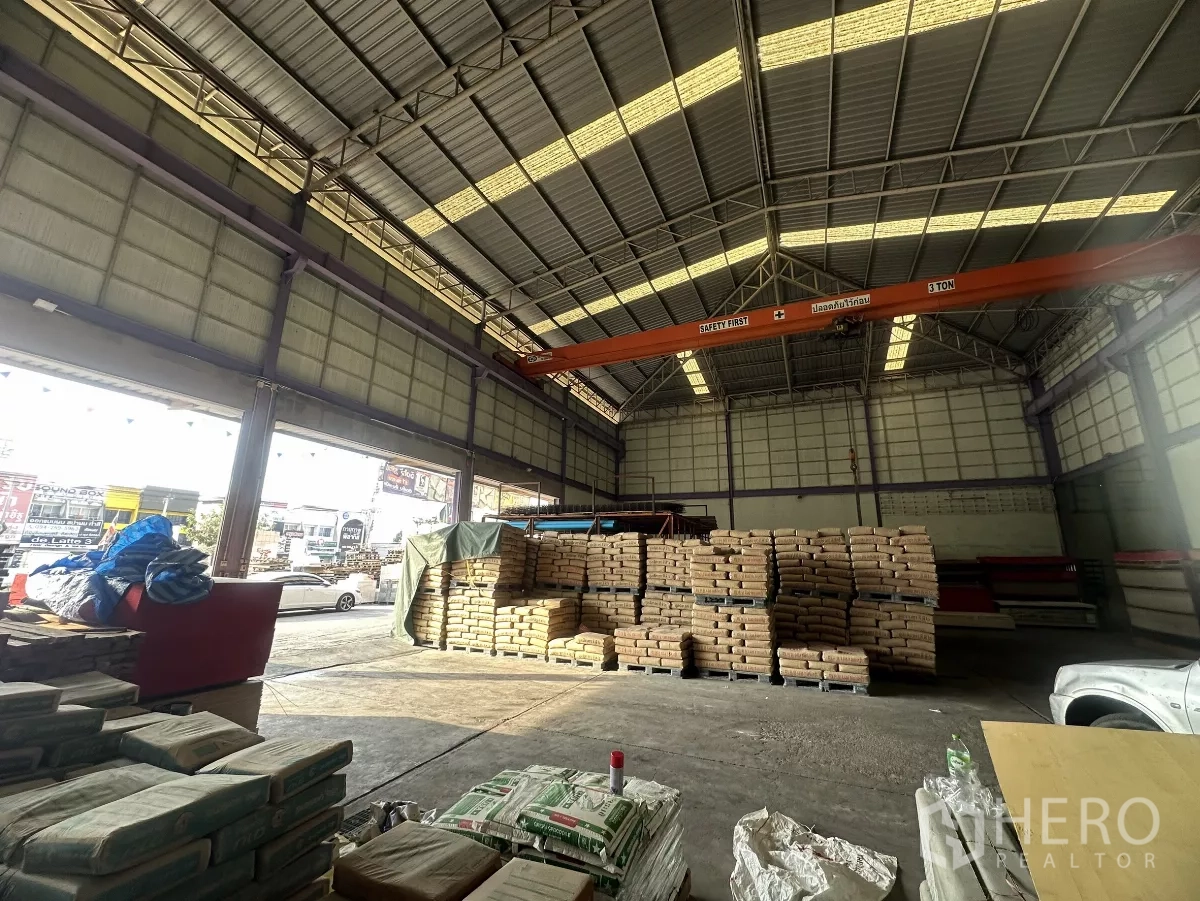 Warehouse for rent in Mueang Nonthaburi, Nonthaburi - High-ceiling warehouse interior with open roller doors, a 3-ton overhead crane and stacked palletized goods.