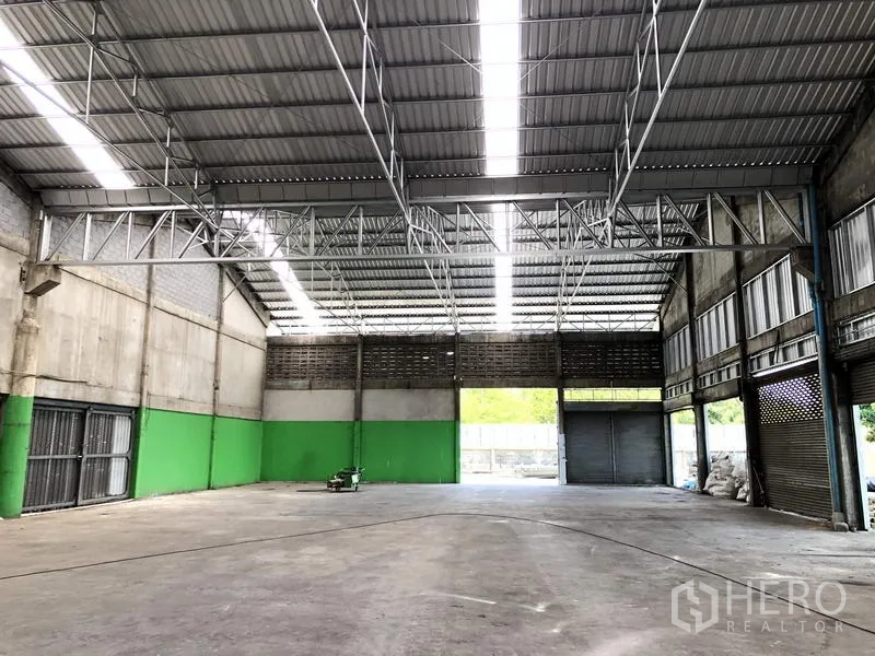 货栈 出租在Pathum Thani - 仓库内部空间开阔，高钢桁架屋顶配采光带，混凝土地面与大卷帘门。
