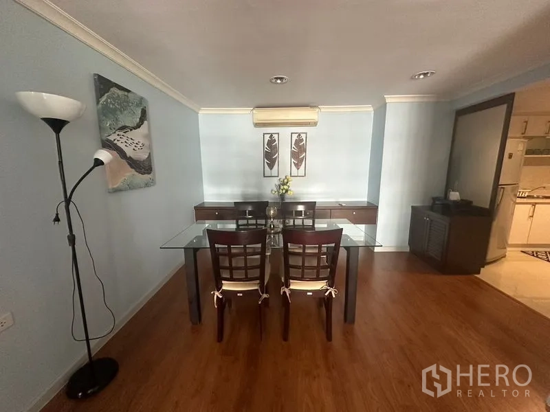 Condominium for rent in Watthana, Bangkok - Glass-top dining table for four on wood flooring with wall art and air conditioning.