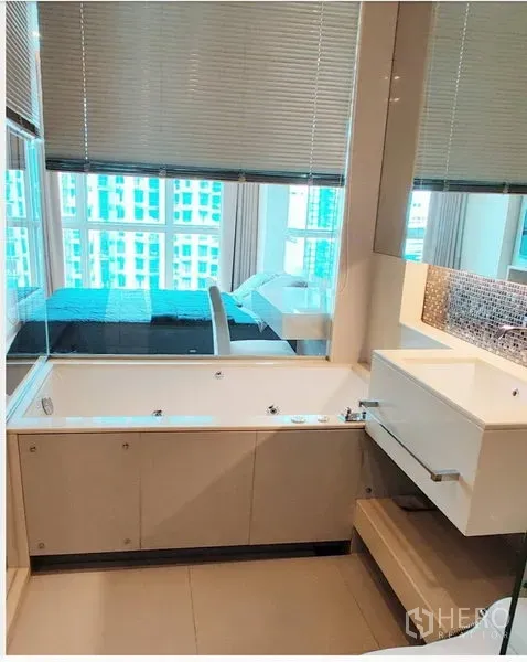 Condominium for rent in Ratchathewi, Bangkok - Modern bathroom with bathtub, large mirror and a glass partition connecting to the bedroom.