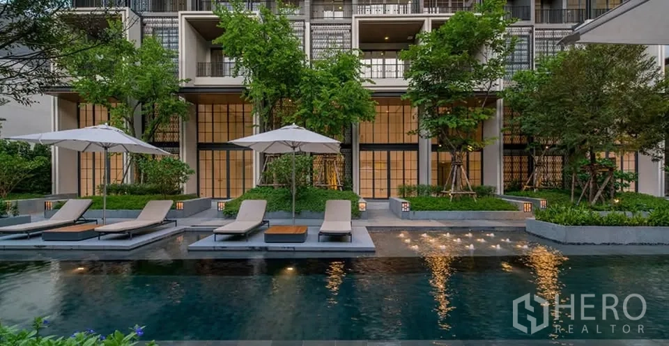 Townhouse for rent or sale in Watthana, Bangkok - Outdoor swimming pool with sun loungers surrounded by greenery.