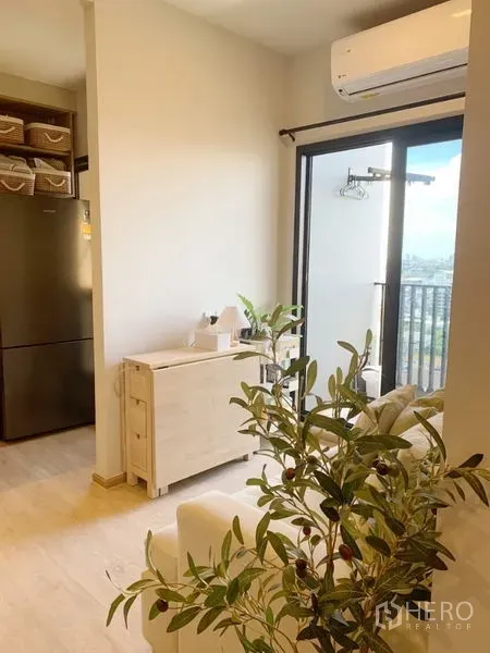 Condominium for sale in Suan Luang, Bangkok - Bright living room with cream sofa, light wood console, air conditioner and sliding glass door to a city-view balcony.