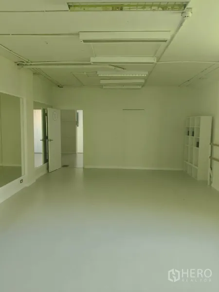 Office Space for rent in Khlong Toei, Bangkok - Open-plan office studio with full mirrors, a shelving unit and doorway to a utility area under bright ceiling lights.