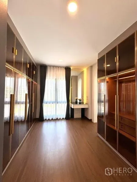 Detached House for rent or sale in Bang Phli, Samut Prakan - Spacious walk-in closet featuring glossy wardrobes with brass handles and a window with drapes.