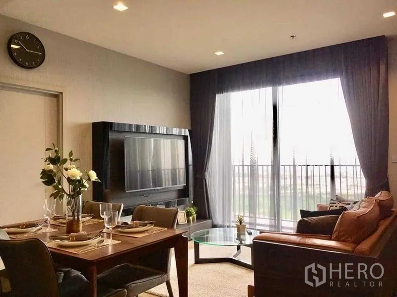 Condominium for rent in Chatuchak, Bangkok - Living area with TV wall unit, dining set and large sliding doors opening to a balcony.