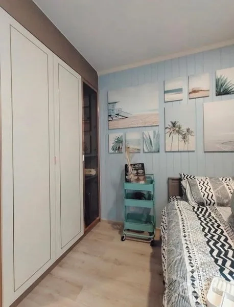 公寓 出租或出售 - 卧室角落有衣柜、海滩主题挂画和滚轮收纳车。