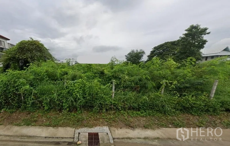 ที่ดิน ให้เช่าในPrawet, Bangkok - ที่ดินเปล่าปกคลุมด้วยต้นไม้ รั้วเตี้ย และท่อระบายน้ำ ติดถนนคอนกรีตในเขตประเวศ กรุงเทพฯ