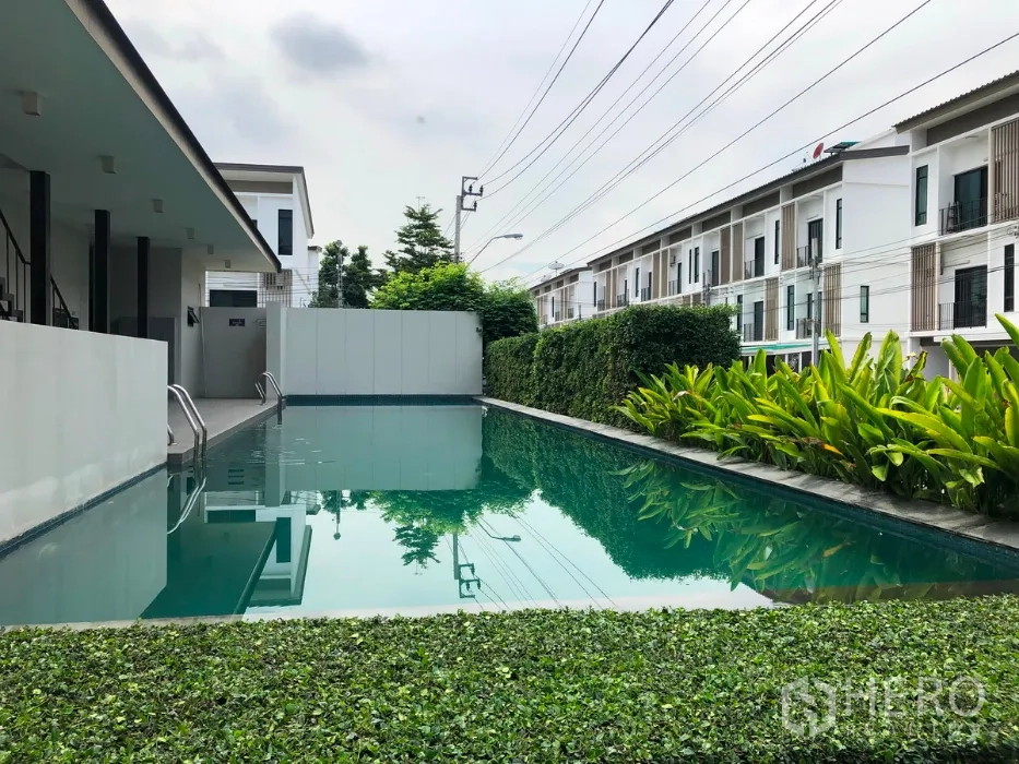 Townhouse for sale in Bang Kapi, Bangkok - Residents’ swimming pool bordered by hedges with townhouse blocks alongside.