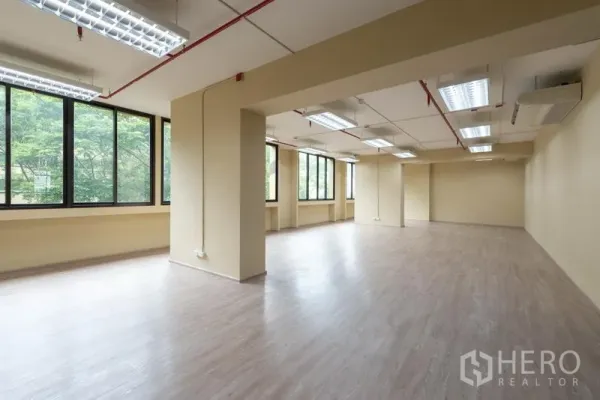 办公空间 出租在Chatuchak, Bangkok - 宽敞开放式办公区，木纹地板、明亮荧光灯，大窗外是绿树景观。