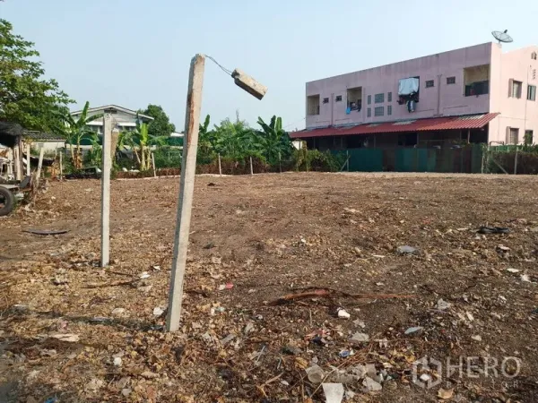 ที่ดิน ขายในKhlong Sam Wa, Bangkok - ที่ดินโล่ง ถมเรียบ มีแนวต้นกล้วย และอาคารสีชมพูด้านหลัง