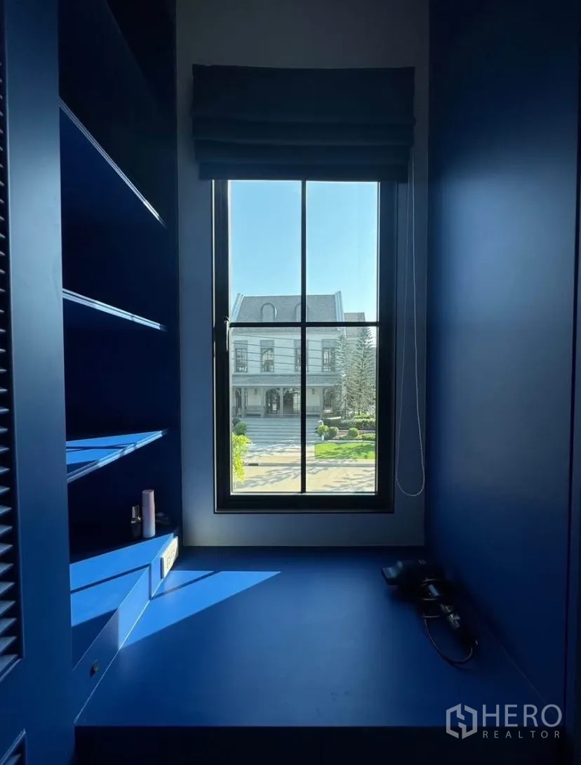 บ้านเดี่ยว for rent or sale in Lat Krabang, Bangkok - มุมหน้าต่างพร้อมชั้นวางบิลท์อินสีน้ำเงินและเบาะนั่ง มองเห็นทางเข้าหมู่บ้าน