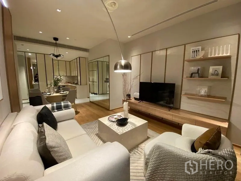 Condominium for rent or sale in Khlong Toei, Bangkok - Open-plan living area with sectional sofa, media wall, dining set and kitchen beyond.