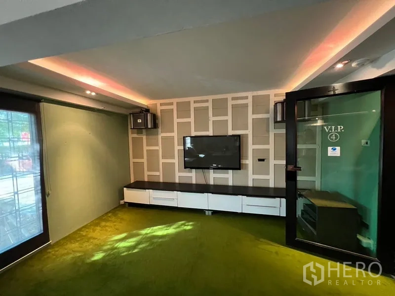 店屋 出租在Suan Luang, Bangkok - 紧凑的VIP影音室，挂墙电视、玻璃门与绿色地毯。