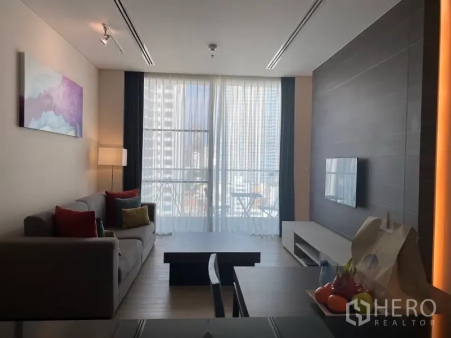 Apartment for rent in Khlong Toei, Bangkok - Bright living room in Nana apartment with sofa, coffee table, wall-mounted TV and city-view balcony.