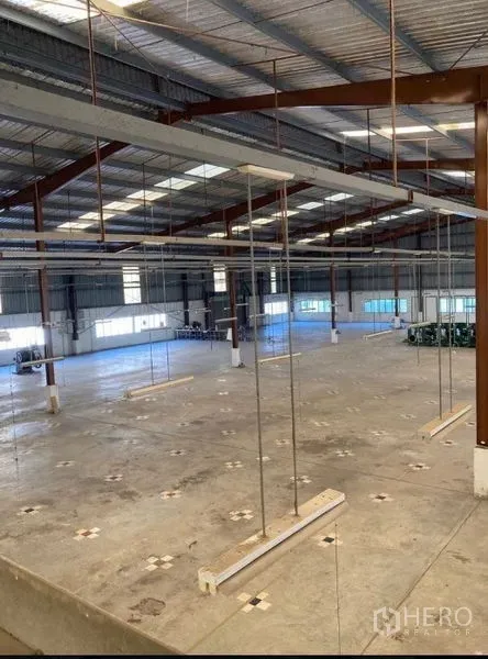 Factory for rent in Song Phi Nong, Suphan Buri - Spacious factory interior with high steel-truss roof, polished concrete floor, suspended light rails and side windows.