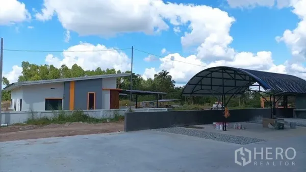 Warehouse for rent in Ban Bueng, Chon Buri - Site view showing a small office building and shaded canopy beside the warehouse yard.