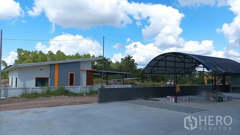 Warehouse for rent in Ban Bueng, Chon Buri - Site view showing a small office building and shaded canopy beside the warehouse yard.