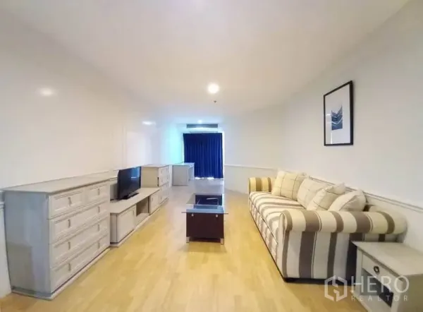 公寓 出租在Khlong Toei, Bangkok - 狭长客厅，配沙发、电视柜、玻璃茶几与遮光窗帘。