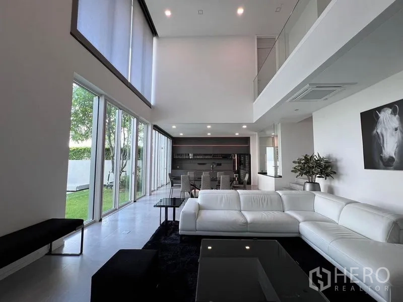 Detached House for sale in Samut Prakan - Double-height living room with floor-to-ceiling glass and a white sectional opening to the garden.
