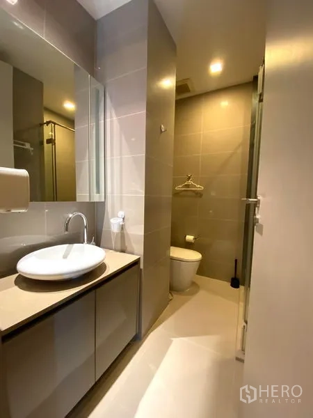 Condominium for rent in Bang Rak, Bangkok - Second bathroom with vanity, mirror, toilet, and shower enclosure.