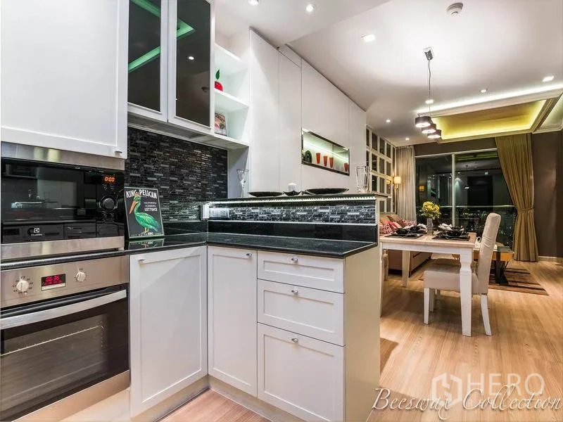 คอนโด ให้เช่าในWatthana, Bangkok - ครัวรูปตัว U สีขาว ท็อปหินแกรนิตสีดำ ผนังกระเบื้องโมเสก พร้อมเตาอบบิวท์อิน มองไปยังพื้นที่ทานอาหาร