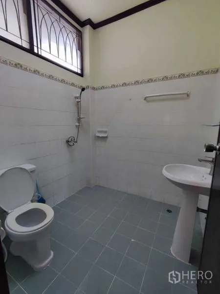 Detached House for rent in Khlong Toei, Bangkok - Simple tiled bathroom with shower, toilet and pedestal sink beneath a high window.