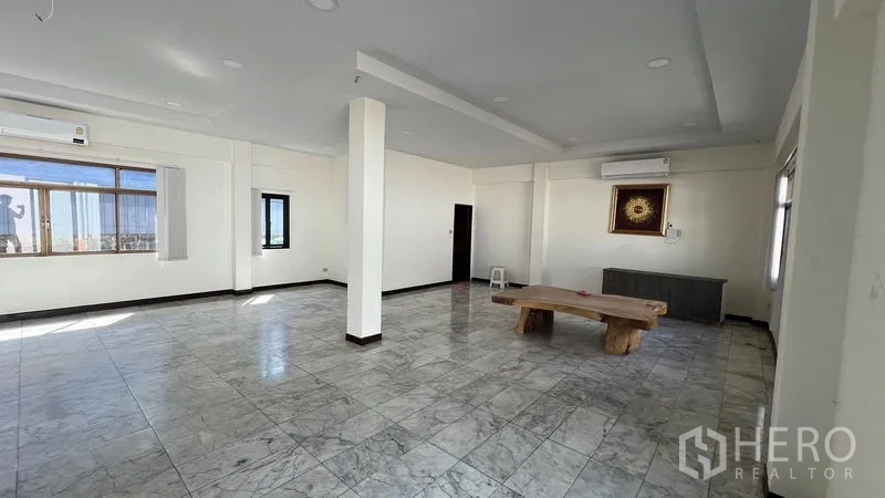 Warehouse for rent in Thanyaburi, Pathum Thani - Open-plan office room with marble-look tiles, air-conditioning units, and a wooden table.