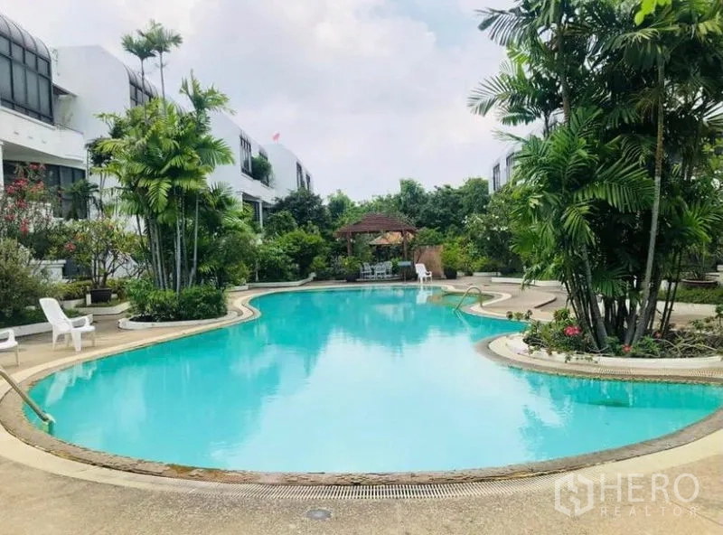 Condominium for rent in Pathum Wan, Bangkok - Resort-style freeform swimming pool with gazebo amid low-rise buildings and palm trees.