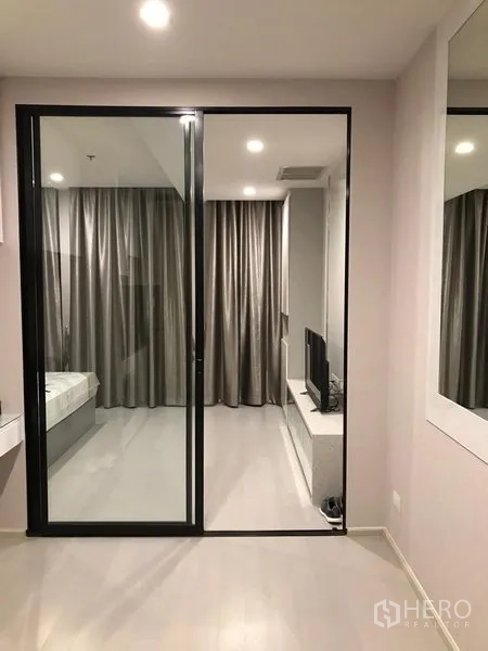 Condominium for rent in Pathum Wan, Bangkok - Glass sliding door separating bedroom and living room with grey curtains