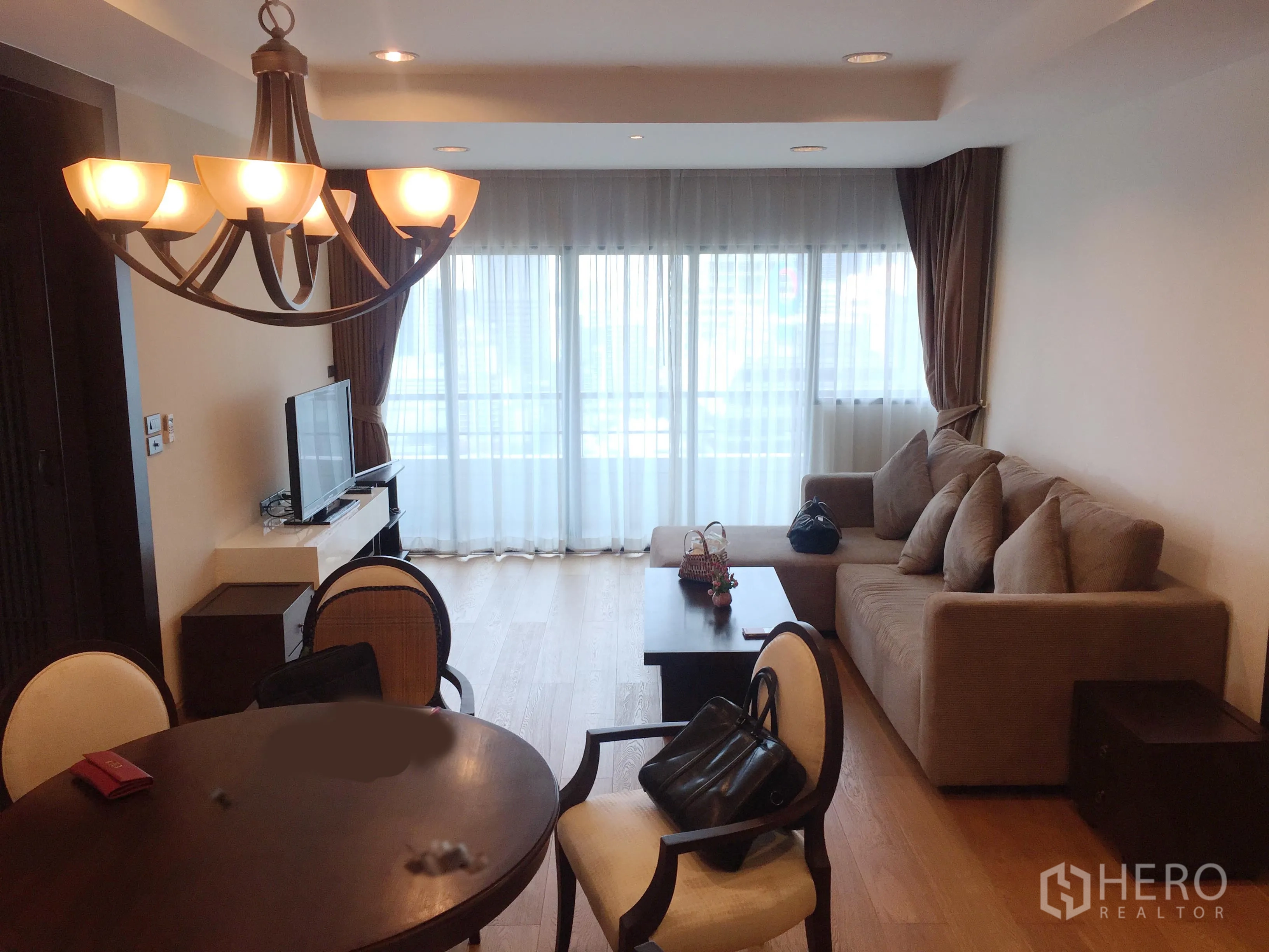 Condominium for rent in Sathon, Bangkok - Bright living and dining area with chandelier, sofa, TV console and floor-to-ceiling windows in a Sathorn condo.