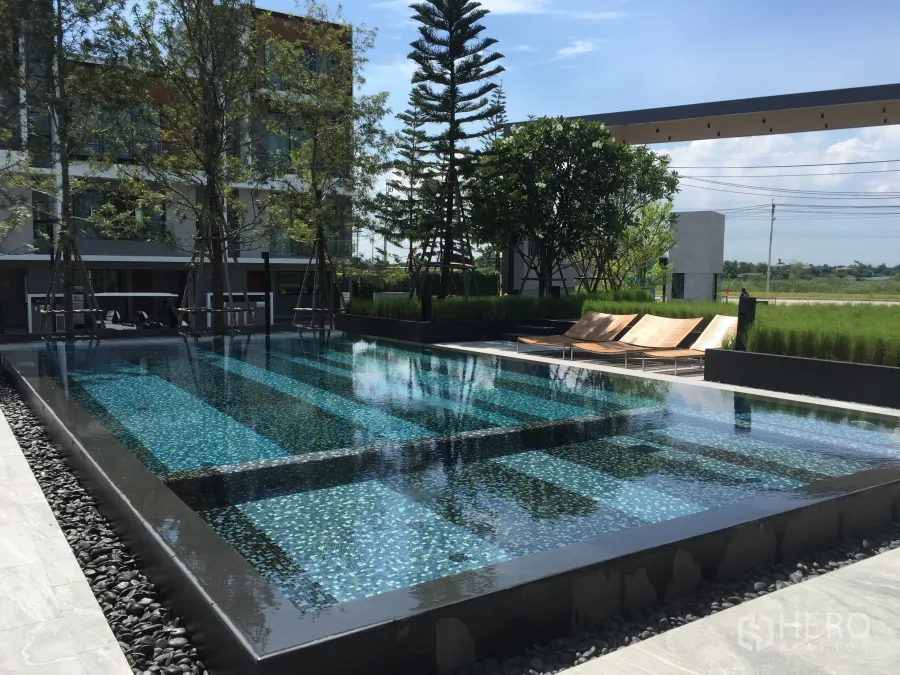 Townhouse for rent in Saphan Sung, Bangkok - Modern communal swimming pool with sun loungers and landscaped garden at a townhouse estate in Saphan Sung.