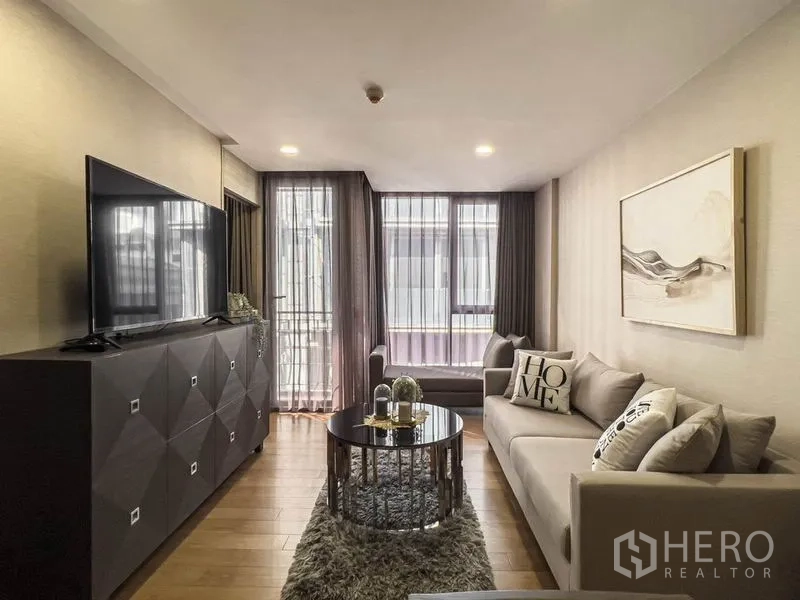 Condominium for rent in Pathum Wan, Bangkok - Long view of the living room toward floor-to-ceiling windows with soft drapes.