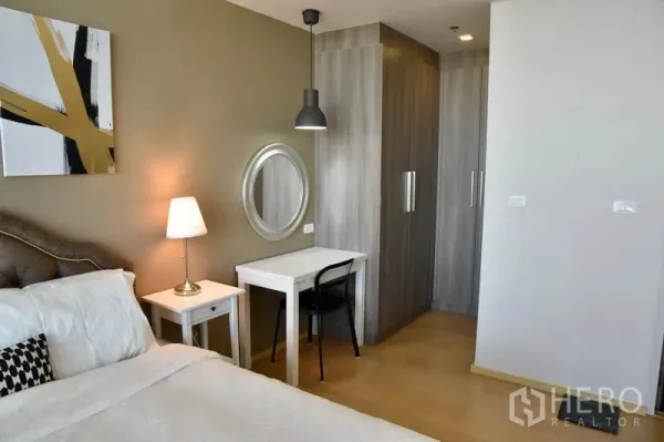 คอนโด ให้เช่าในPhaya Thai, Bangkok - มุมห้องนอนมีโต๊ะทำงาน กระจกแขวน ตู้เสื้อผ้า และโคมไฟหัวเตียงแสงอบอุ่น.