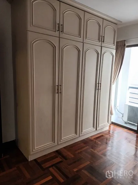 คอนโด ให้เช่าในDin Daeng, Bangkok - ตู้เสื้อผ้าสีครีมทรงสูงในห้องนอน ข้างระเบียง บนพื้นปาร์เกต์เงางาม
