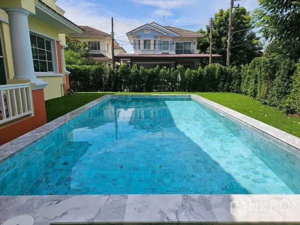 Detached House for rent in Thanyaburi, Pathum Thani - Crystal-clear pool bordered by manicured hedges with neighboring homes in the background.