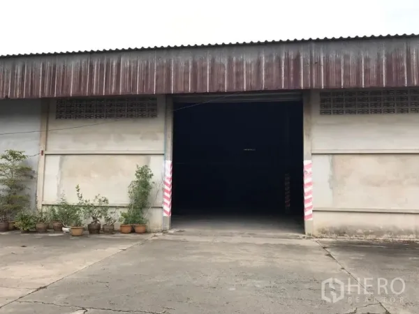 货栈 出租在Mueang Nakhon Pathom, Nakhon Pathom - 仓库正立面，宽入口与混凝土场地，摆放盆栽