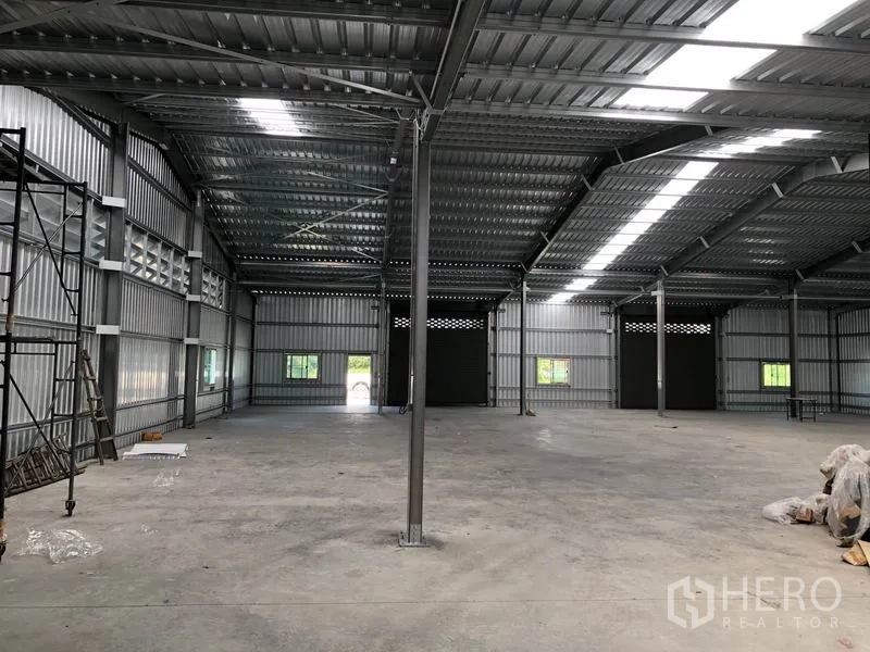 Warehouse for rent in Pak Kret, Nonthaburi - Interior view toward loading doors with scaffolding and visible power points.